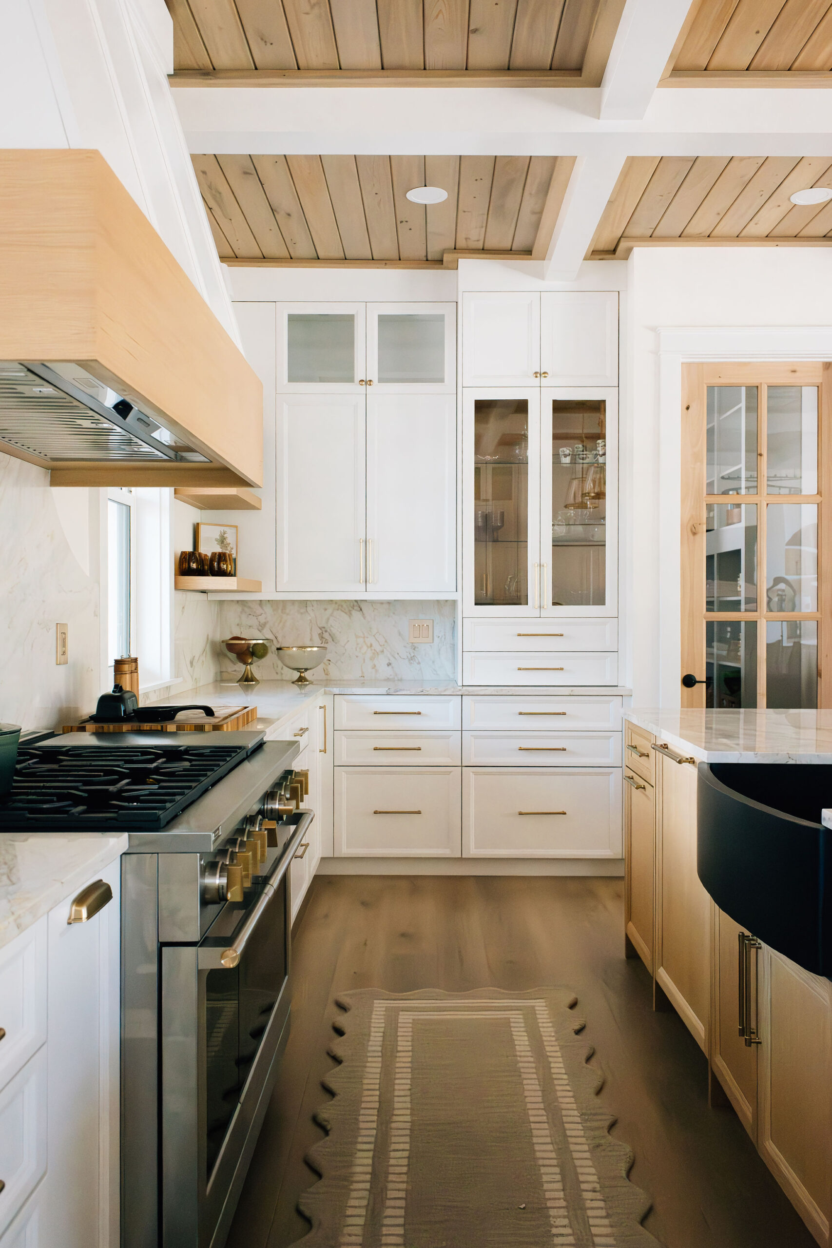 RDM Interiors Bradenton Designer New Construction. Transitional kitchen with white shaker cabinetry, brass hardware, marble backsplash, a professional gas range, light wood floors, and a coffered shiplap ceiling — RDM Interiors